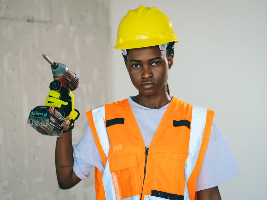 A determined construction worker holding a drill in safety gear indoors.